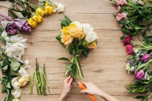 cropped-view-of-florist-cutting-flower-stalks-in-bouquet-on-wooden-surface